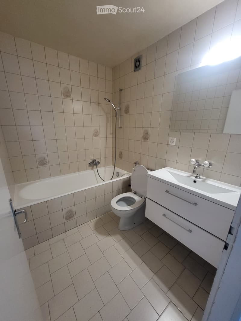 Bathroom with a bathtub, toilet, sink, and showerhead. The walls and floor are tiled, and the sink has a modern faucet.