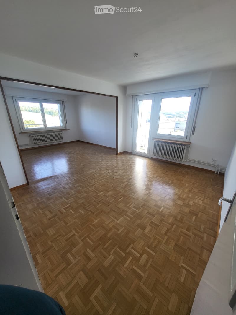 Empty room with wooden herringbone flooring, white walls, large windows, and radiators. No furniture or equipment present.