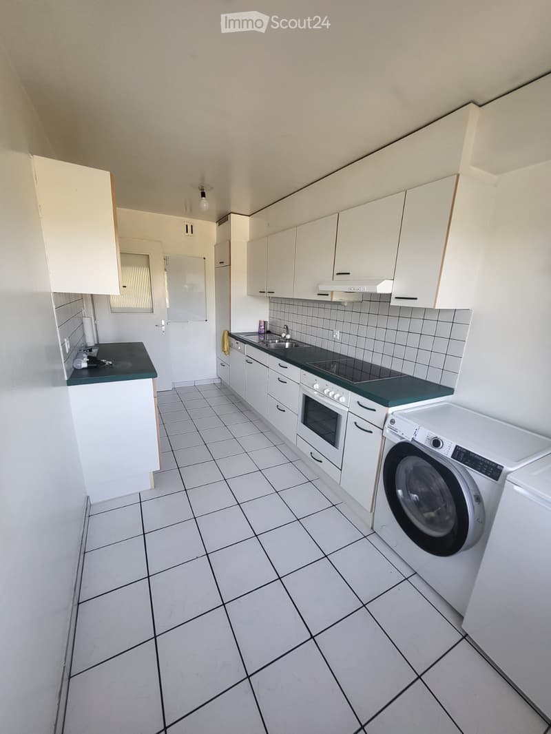 Modern kitchen with white cabinets, tiled floor, oven, washing machine, sink, and countertop.