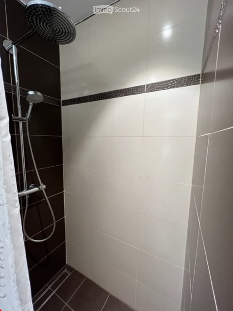 White and black tiled walls, curved shower head, and a clear shower curtain