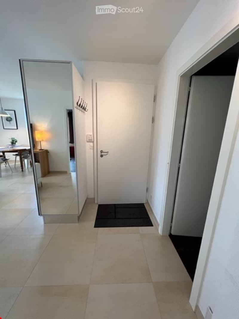 empty room with entrance, full length mirror, hallway with tiled floor, white wall, lamp and table in mirror's reflection