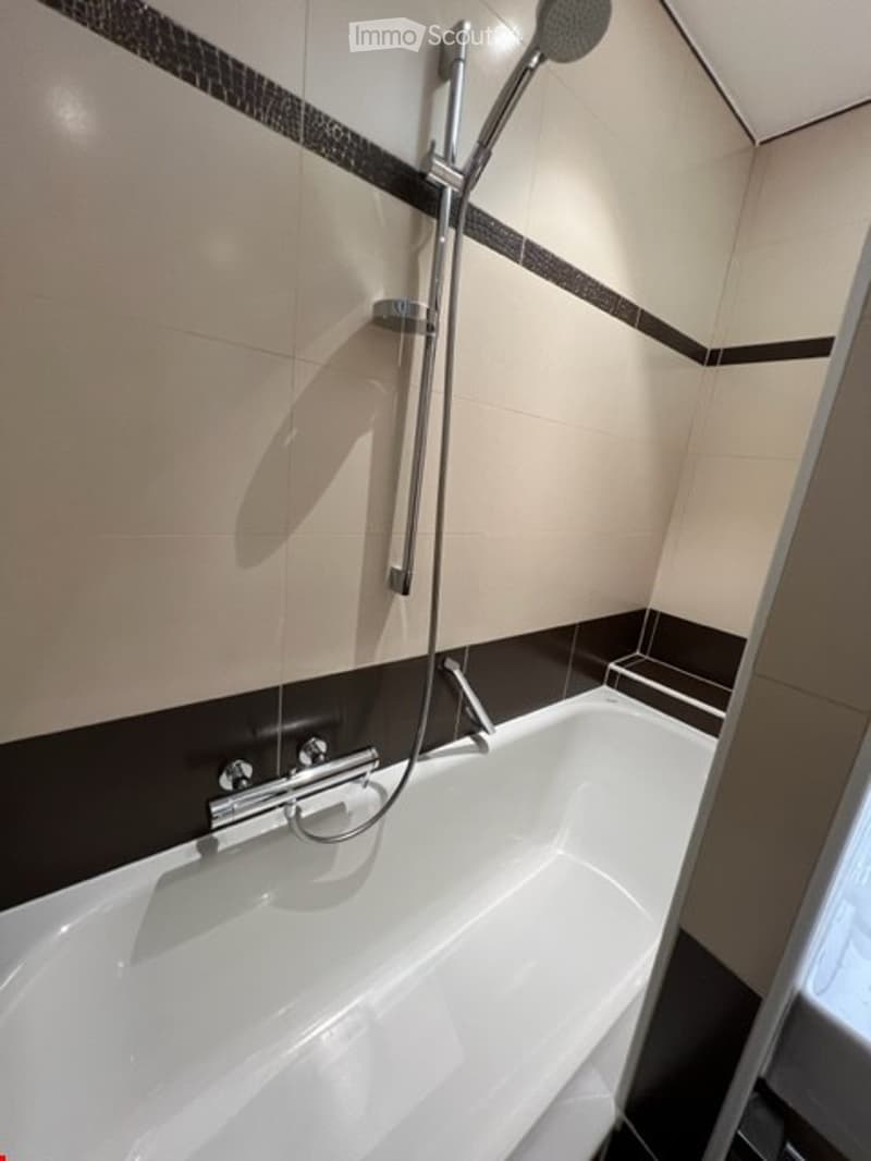 Bathroom with bathtub and shower, white tiles and black accents
