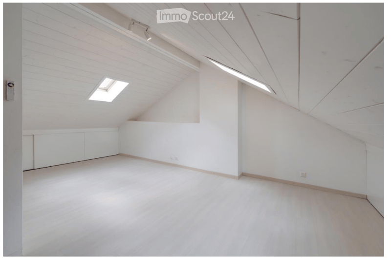 Bright, empty attic room with white walls, wooden floor, skylight window, and built-in white cabinetry along one wall.
