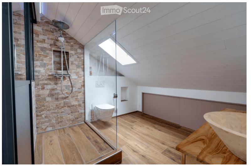 Modern bathroom with wooden flooring, exposed brick wall, glass-enclosed shower, and a sleek toilet.