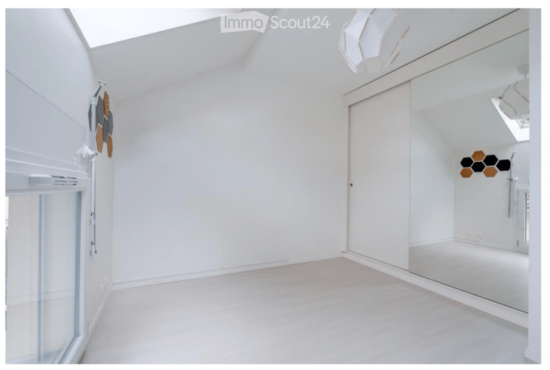 Completely empty room with white walls, light-colored flooring, and a large mirror on one wall. The room features a skylight and a sliding glass door leading to an outdoor area.