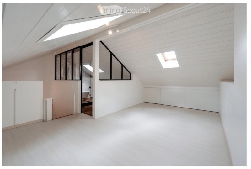 Bright, empty attic space with white walls, wooden floor, large windows, and skylights.