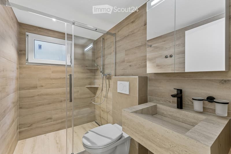 Modern bathroom with wooden walls and floor, glass shower enclosure, toilet, sink, and mirrored cabinet.