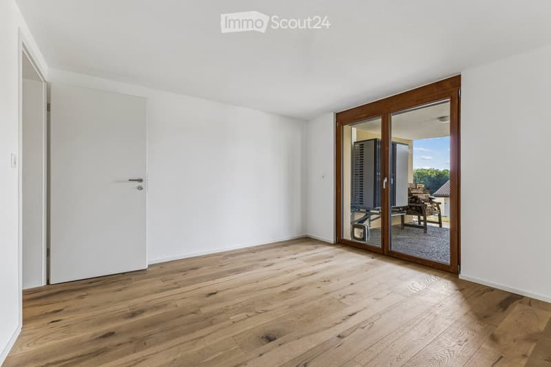 Empty room with light wooden flooring, white walls, and a large sliding glass door leading to an outdoor area.