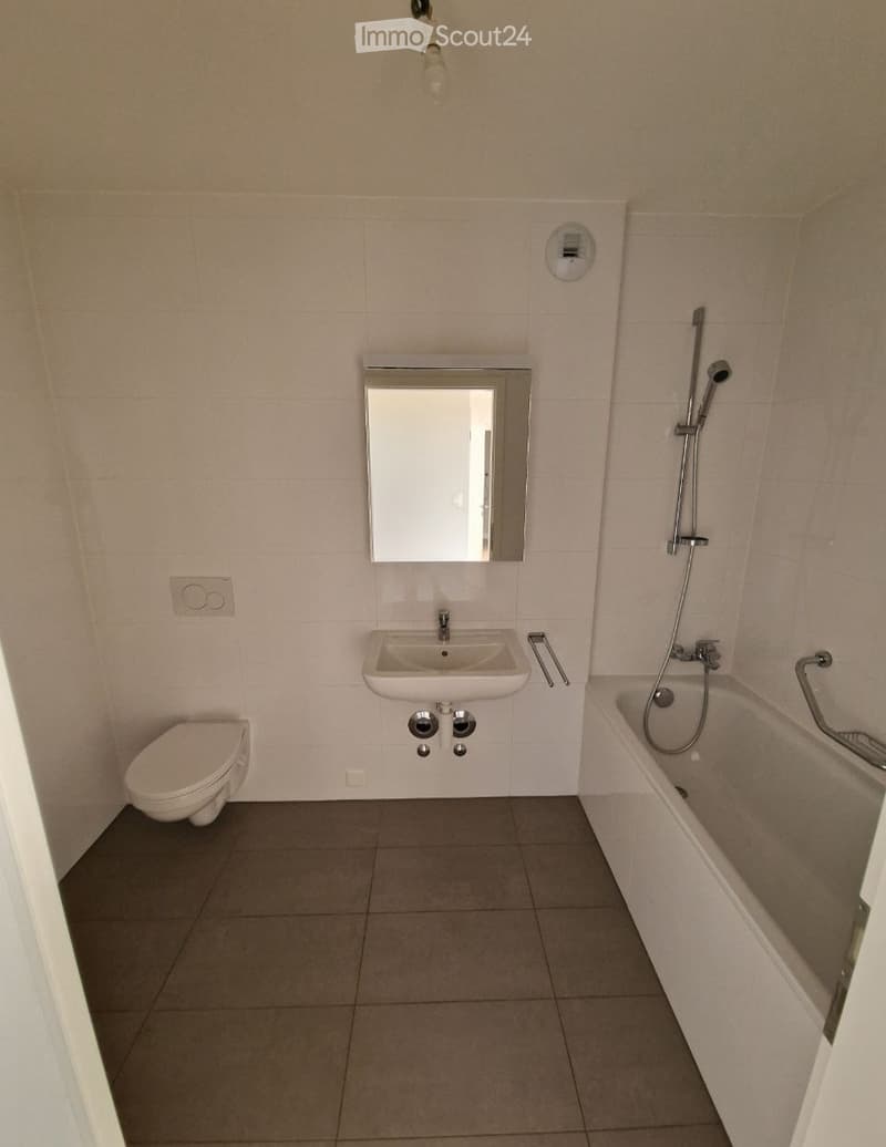 Modern bathroom with a toilet, sink, bathtub, and mirror. Light-colored tiles and a neutral color scheme.