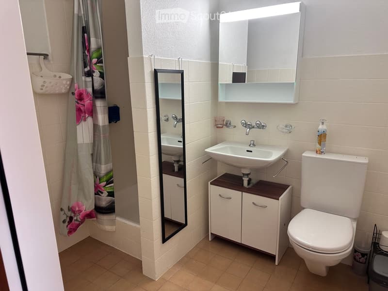 Modern bathroom with a white sink, toilet, mirrored cabinet, and a shower area with a floral curtain.