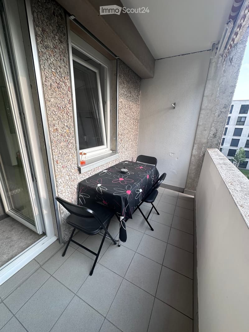 Balcony with tiled floor, small table with floral tablecloth, and two black folding chairs.