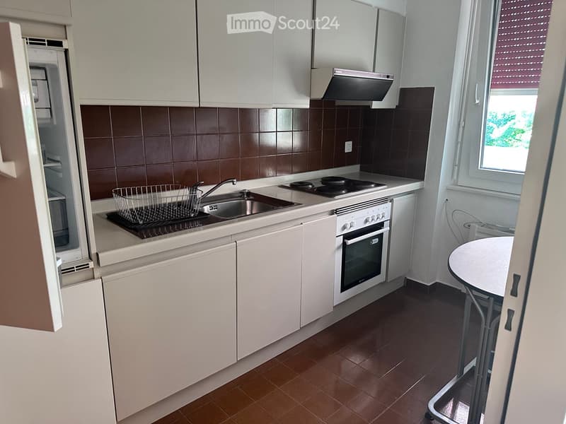 Modern kitchen with white cabinets, stainless steel appliances, and a small round table near the window.