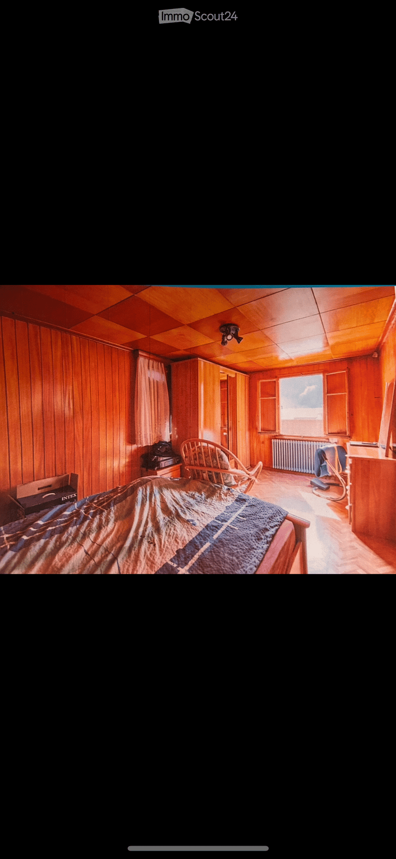 bedroom with wooden walls, bed, chair, desk, radiator, window
