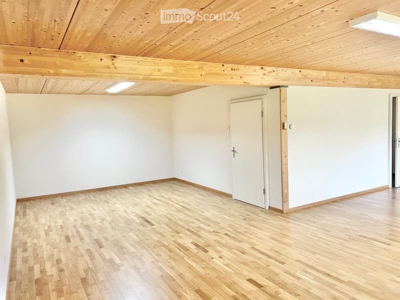 Empty room with wooden flooring, white walls, and exposed wooden ceiling beams. Features a single door and recessed lighting.