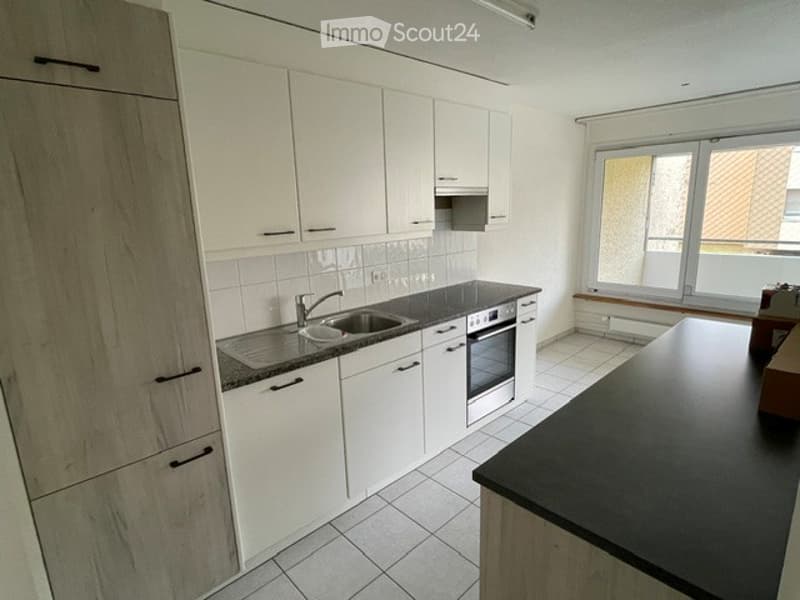 Modern kitchen with white cabinets, black countertop, stainless steel sink, and built-in oven. Large window provides natural light.