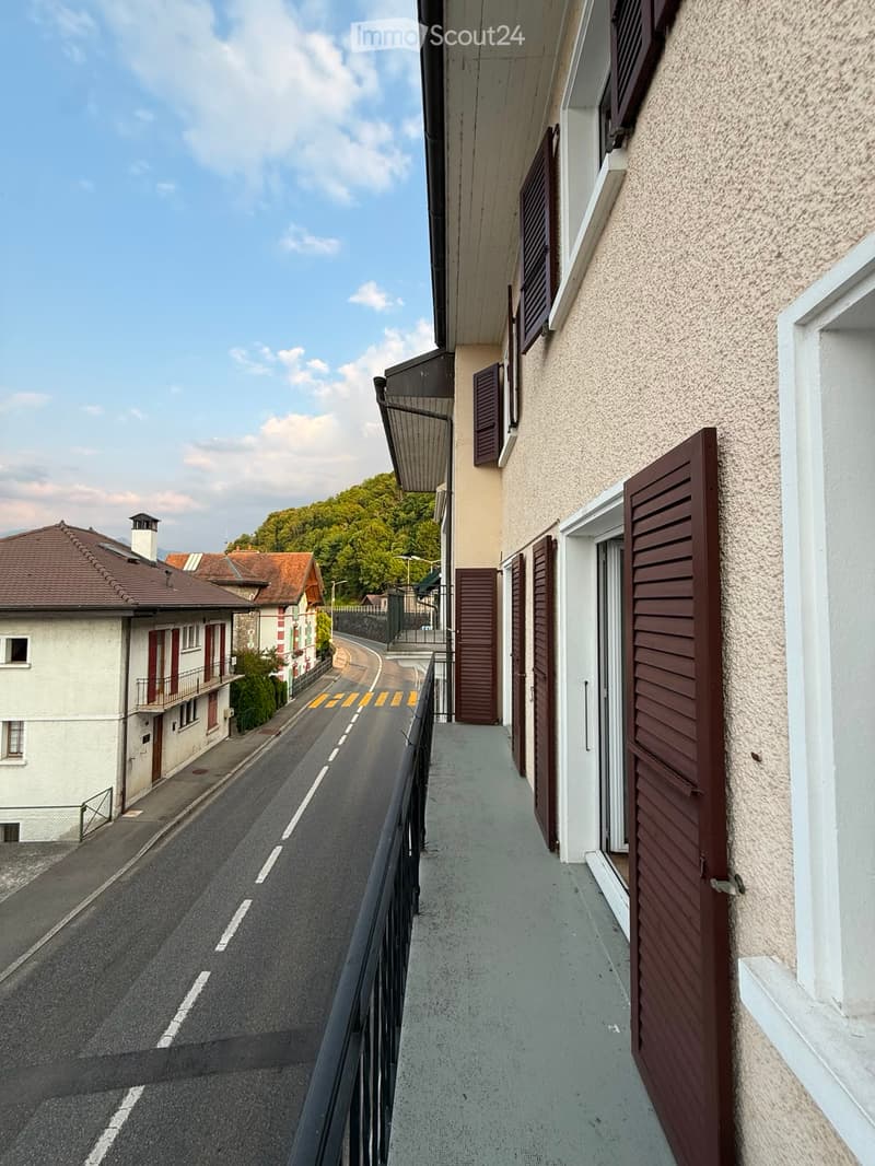 Balcony overlooking a narrow street with buildings and a view of greenery in the distance.