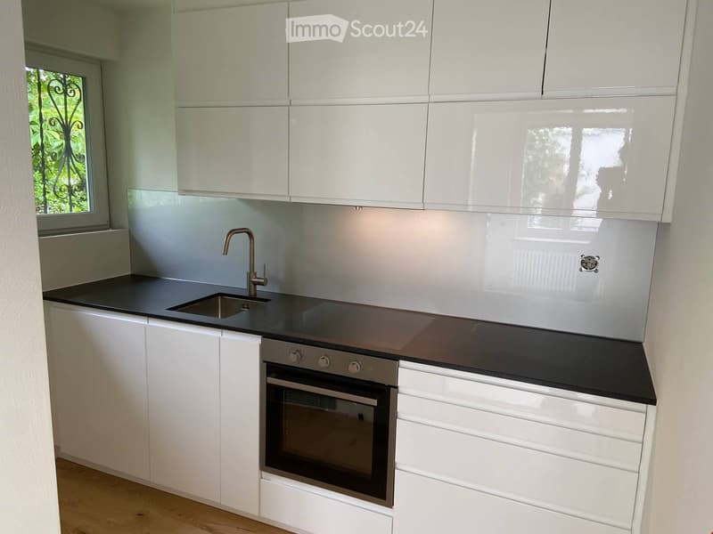 modern kitchen with white cabinets, black countertops, stainless steel sink, oven, and faucet, glass backsplash, wooden floor