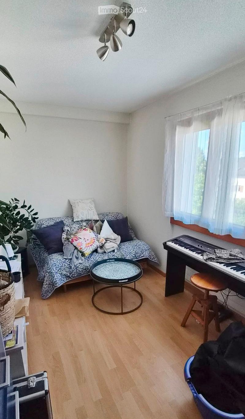 A cozy living room with a patterned sofa, coffee table, piano, and a small plant near the window.