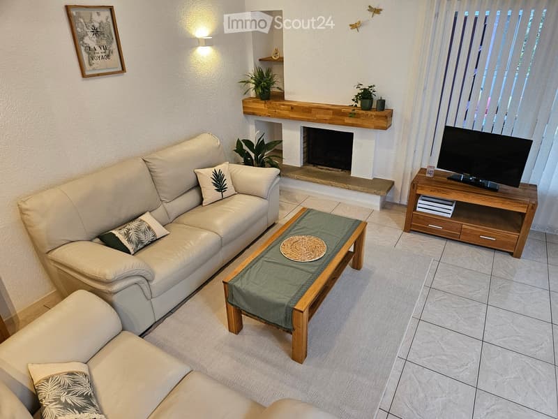Modern living room with a white leather sofa, coffee table, fireplace, TV, and decorative plants.