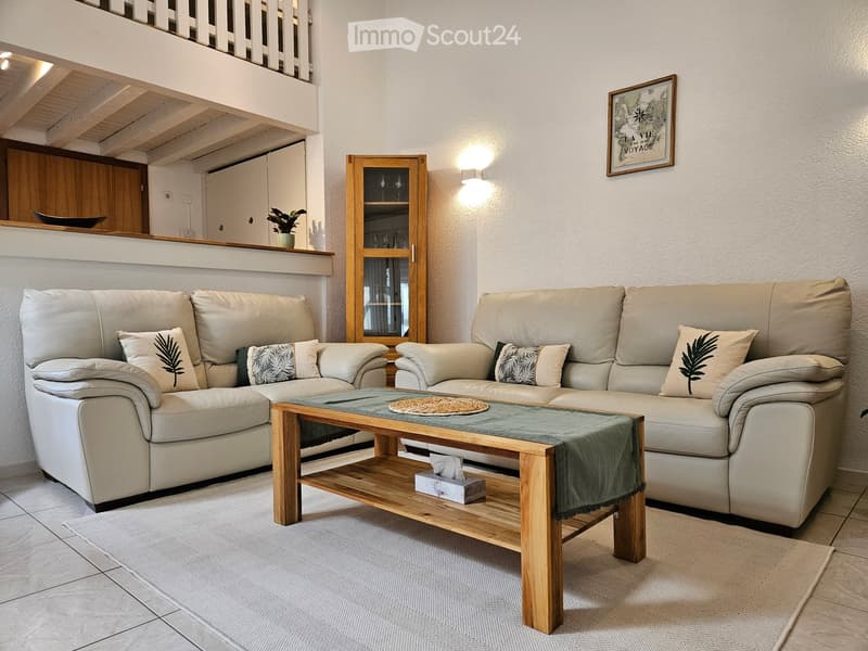 Modern living room with two beige sofas, a wooden coffee table, a cabinet with glass doors, and a small plant on the shelf.