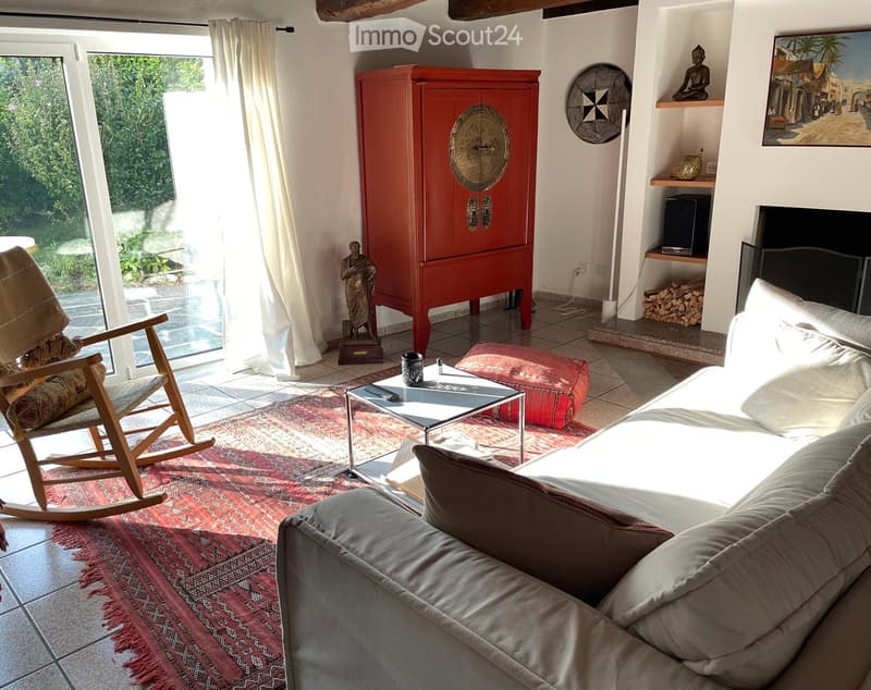 Living room with a grey sofa, coffee table, rocking chair, red cabinet, and decorative items including a statue and a painting.