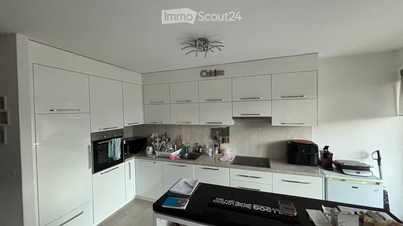 Modern kitchen with white cabinets, stainless steel appliances, and a black countertop. Visible items include an oven, microwave, sink, fridge, coffee maker, toaster, induction hob, and various kitchen utensils.