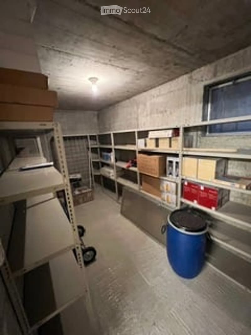 Empty storage room with metal shelving units, cardboard boxes, and a large blue container on the floor.