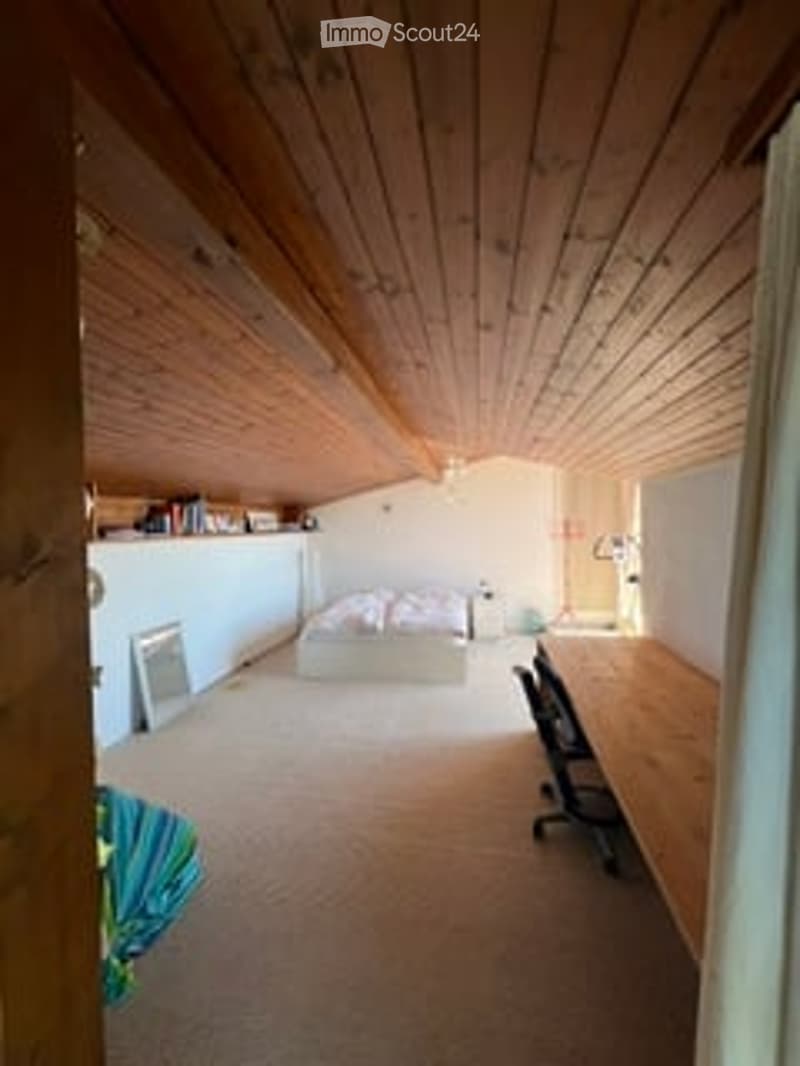 Empty attic bedroom with wooden slanted ceilings, carpeted floor, and exposed wooden beams. No furniture or equipment present.
