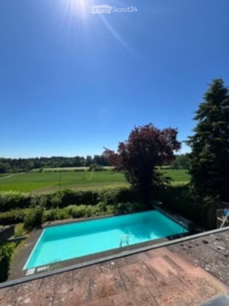 A rooftop terrace with a swimming pool, surrounded by greenery and a scenic countryside view.