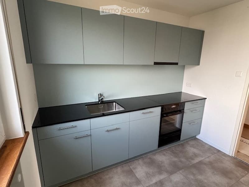 modern kitchen with gray cabinets, black countertops, stainless steel sink, built-in oven, and a wooden window sill