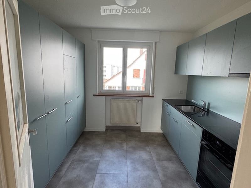 empty kitchen with gray cabinets, black countertop, white radiator, stainless steel sink, oven