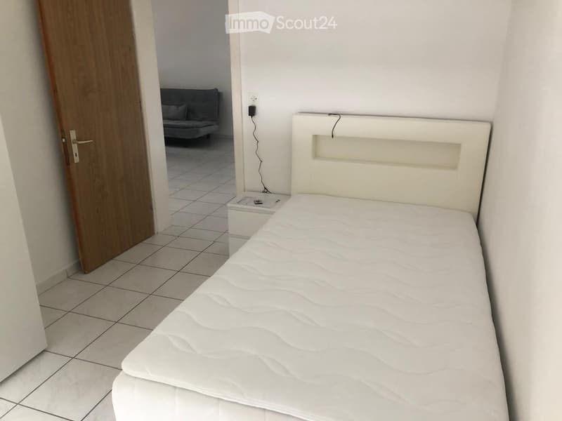 single bed with headboard, bedside table, electrical outlet, door leading to another room with a couch