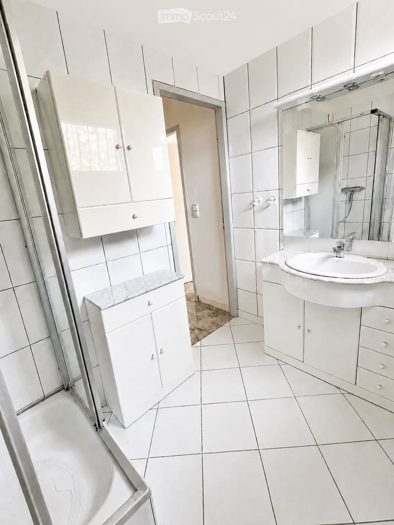 Modern bathroom with white tiles, a sink, cabinets, and a mirror. The space is clean and well-organized.