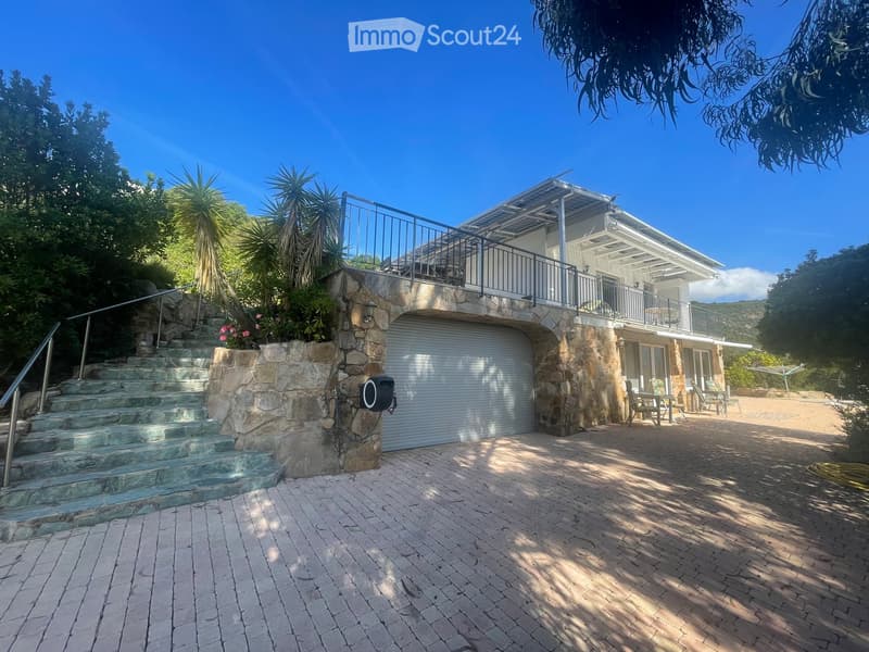 Two-story house with a stone facade, garage, outdoor patio, and balcony overlooking a scenic view.