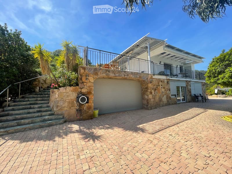 Two-story house with a stone facade, garage, balcony, and outdoor seating area. The entrance features stone steps leading up to the house.