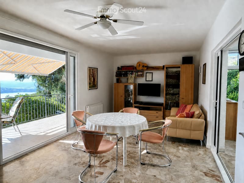 Bright living room with a view, featuring a white ceiling fan, a round table with chairs, a sofa, a television, and a guitar on a shelf.