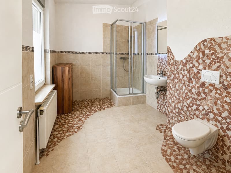 Modern bathroom with beige tiles, a glass-enclosed shower, a toilet, a sink, and a wooden cabinet.