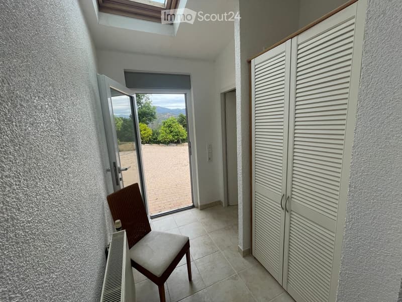 A hallway with a tiled floor, a wooden chair, a white wardrobe, and a sliding glass door leading to an outdoor patio.
