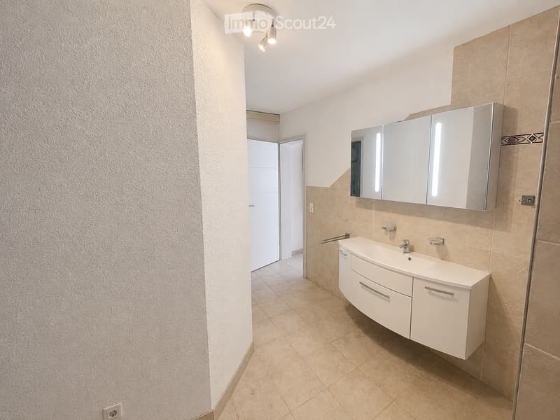 Modern bathroom with beige tiles, white sink cabinet, large mirror, and recessed lighting.