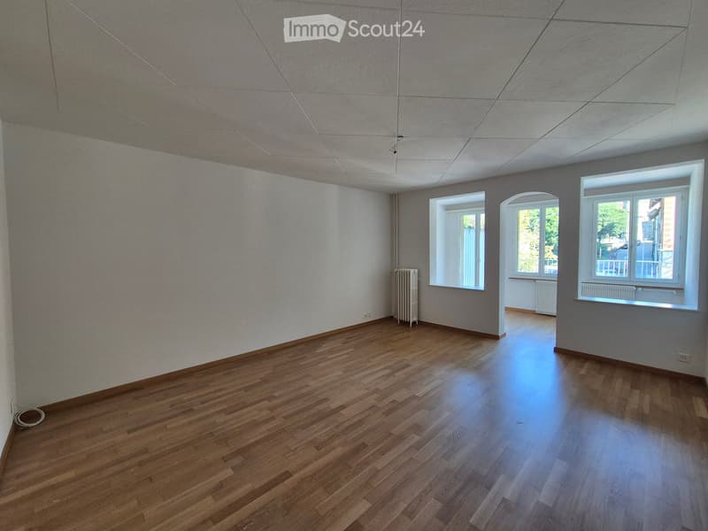 Empty room with wooden flooring, white walls, and three windows allowing natural light. Radiators are visible near the windows.