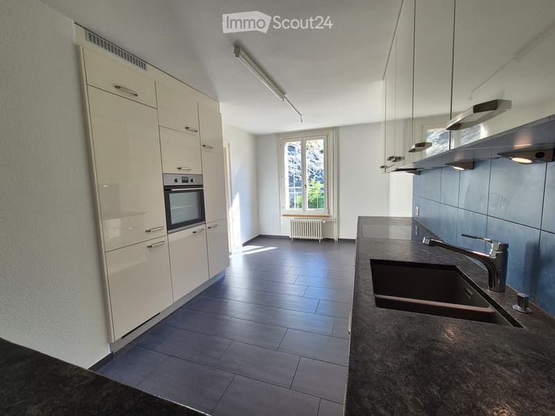Modern kitchen with white cabinets, dark granite countertop, stainless steel sink and faucet, built-in oven, and a window with a view of greenery.