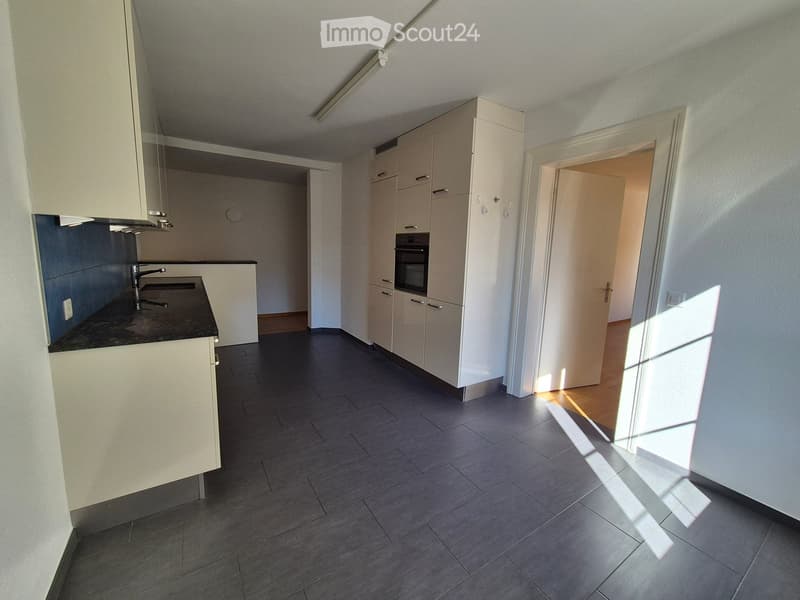 Modern kitchen with white cabinets, dark countertops, and a sink. The floor is tiled, and there is a doorway leading to another room.