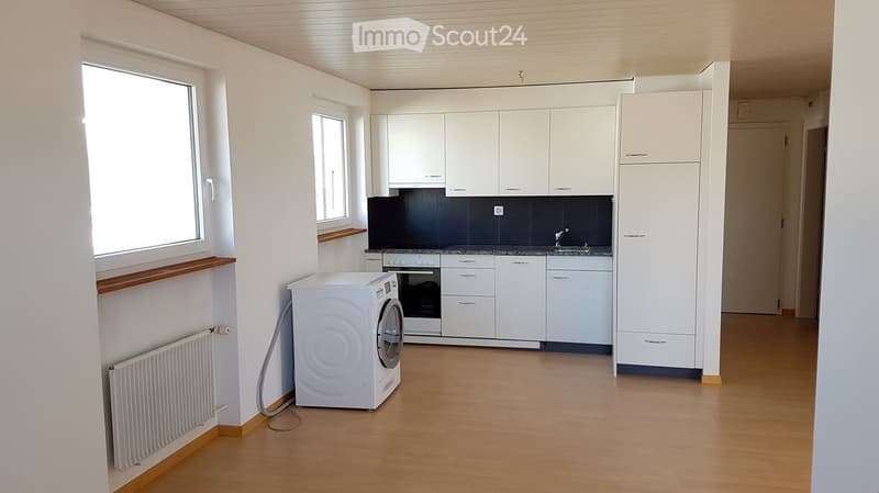 Bright kitchen with white cabinets, a washing machine, an oven, and a sink, featuring wooden flooring and large windows.