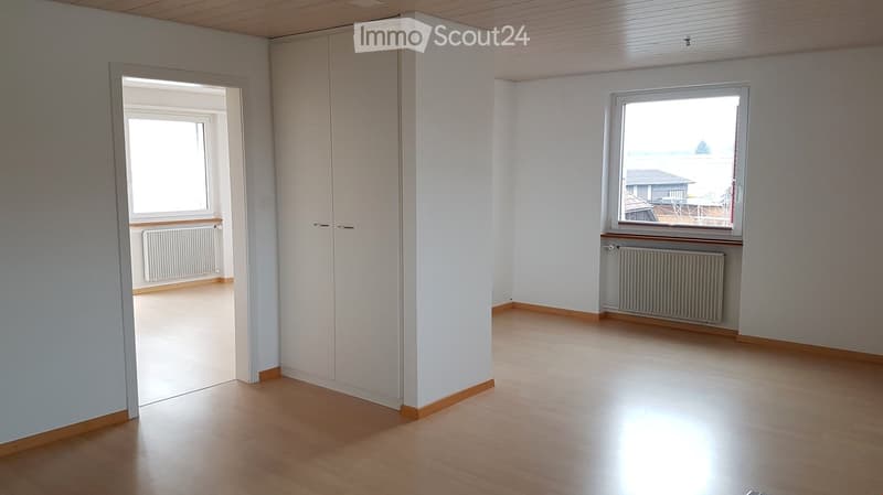 Empty room with wooden flooring, white walls, and large windows offering a view of the water. Features include radiators and a closet.