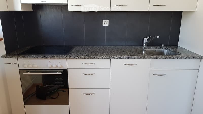 Modern kitchen with white cabinets, granite countertop, built-in oven, and stainless steel sink with faucet.