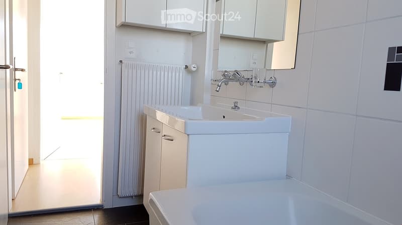 Modern bathroom with white tiled walls, a white sink with a chrome faucet, a bathtub, a mirror, and a cabinet.