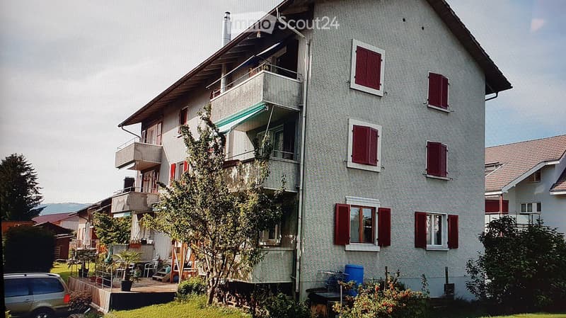 Multi-story residential building with balconies, red shutters, and a green awning on the upper level.