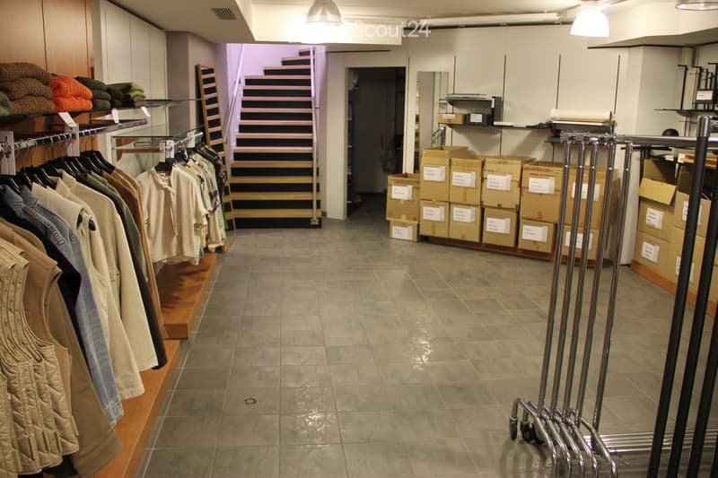 Retail space with tiled floor, clothing racks, shelves with folded blankets, and stacked boxes.