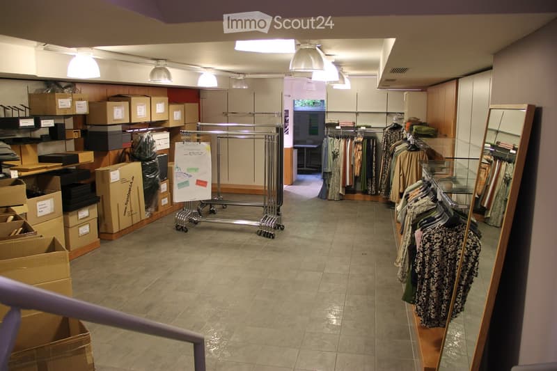 Retail space with tiled floor, clothing racks, large mirror, and several cardboard boxes stacked along the walls.