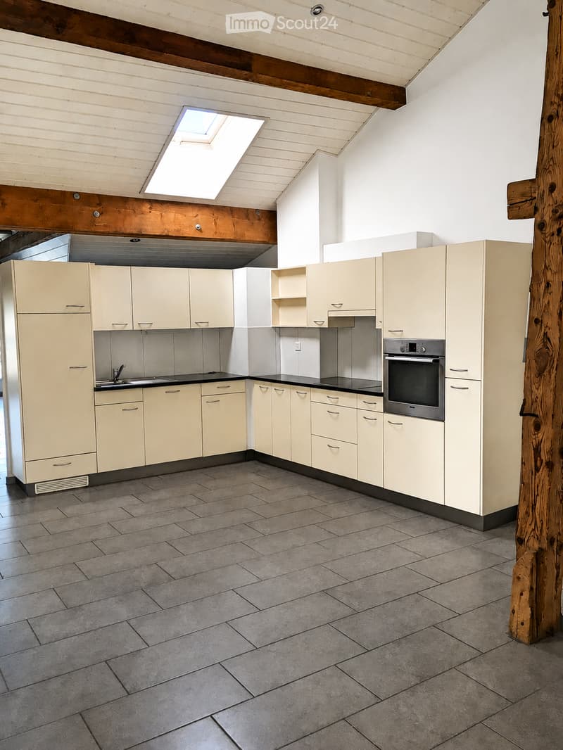 Modern kitchen with light-colored cabinets, stainless steel oven, and tiled floor. Features a skylight window and exposed wooden beams on the ceiling.